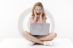 Scared terrified young cute caucasian blond girl scream from fear, sit crossed legs hold laptop, close eyes and shouting
