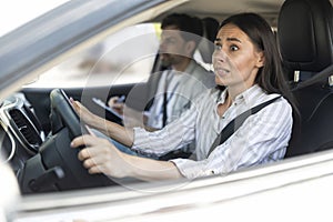 Scared unconfident woman driving car with instructor by her side