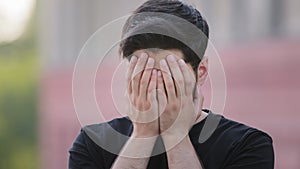 Scared upset middle eastern bearded young man wearing black t-shirt cover face feel frightened, fearful Indian male