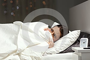 Scared woman hiding under blanket on a bed in the night