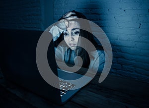 Scared woman on laptop in the dark feeling fear suffering online harassment and cyberbullying