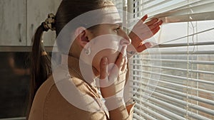 Scared woman saw crime on street through window blinds. Crime witness, spying through window, peeking on street.