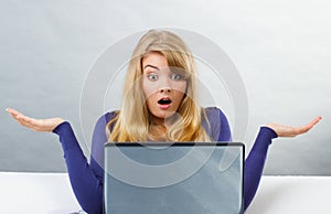 Scared woman shrugging shoulders and looking at laptop, computer problem