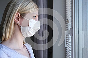 Scared woman in surgical face mask staying at home and looking through the window, covid-19 quarantine and self isolation, photo