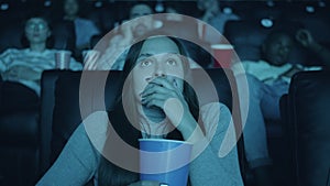 Scared woman watching horror film with open mouth holding popcorn in cinema