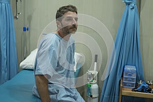 Scared and worried man hospitalized - attractive injured man sitting on hospital bed receiving treatment feeling sick and unwell