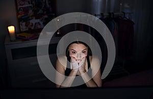 Scared and worried young girl with laptop sitting indoors, internet abuse concept.