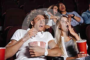 Scared young friends sitting in cinema watch film