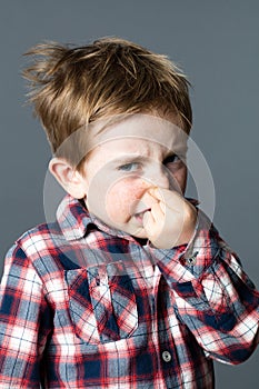 Scared young kid pinching his nose annoyed by bad odor photo