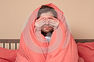 Scared young man covering face in stress sitting in bed