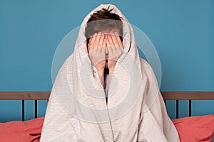 Scared young man covering face in stress sitting in bed