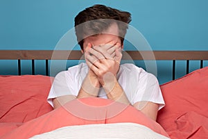 Scared young man covering face in stress sitting in bed