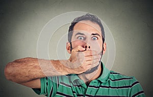 Scared young man covering with hand his mouth