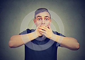 Scared man with hands covering mouth anxiously looking at camera