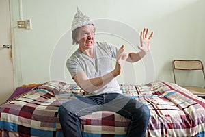 Scared young man with tin foil hat feeling terrified in the bedroom