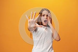 Scared young teen girl showing stop gesture against yellow background