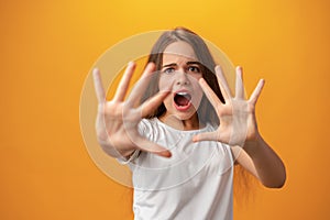 Scared young teen girl showing stop gesture against yellow background