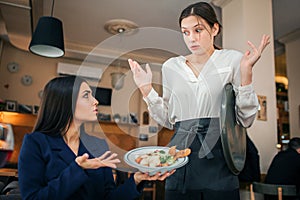 Scared young waitress look at salad bowl brunette hold in hands. She show her this food. Young woman in blouse is photo