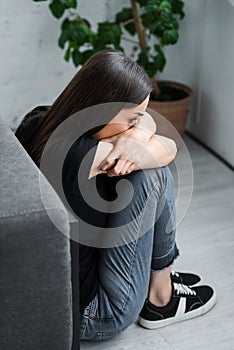 scared young woman hiding face in crossed arms while sitting on floor and suffering from panic attack.