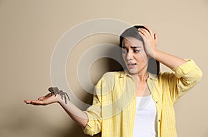 Scared young woman holding tarantula on beige. Arachnophobia fear of spiders