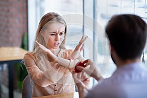 Scared young woman rejecting marriage proposal, gesturing NO, refusing to accept engagement ring at cafe