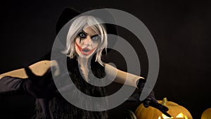 Scary beautiful girl witch celebrates halloween with funny glowing burning pumpkins in smoke. Woman with gray hair