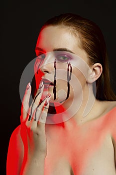 Scary beauty Halloween makeup portrait of a beautiful red hair girl with red eye shadows and fake blood from yellow eyes