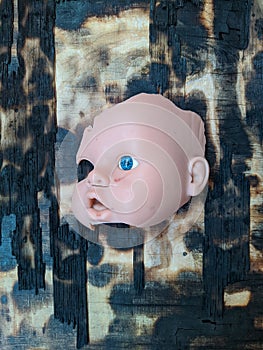 scary and broken doll face with one blue eye on a background of burnt wooden board