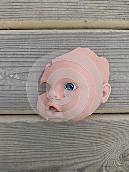 scary and broken doll face with one blue eye on a background of gray wooden background
