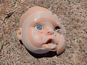 scary and broken doll face with one blue eye on a background of stone