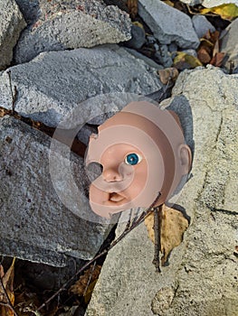 scary and broken doll face with one blue eye on a background of stones and autumn leaves in the daytime