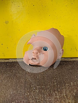 scary and broken doll face with one blue eye on a background of yellow and wooden background