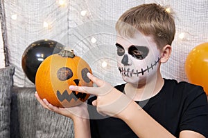 Scary child with a make-up in form of a skeleton and with a pumpkin in his hands