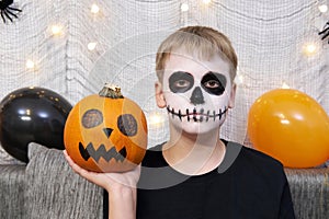 Scary child with a make-up in form of a skeleton and with a pumpkin in his hands