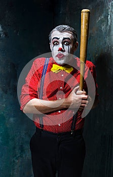 The scary clown and baseball-bat on dack background. Halloween concept