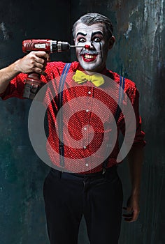 The scary clown and electric drill on dack background. Halloween concept