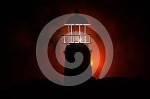 Scary dark ominous lighthouse behind a red fire background. Lighthouse at dusk/ Sunset Light House/ Light house at sunset. Decorat