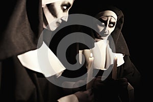 Scary devilish nun with burning candle near mirror on black background. Halloween party look