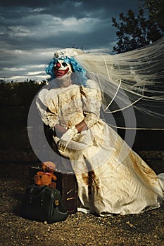 Scary evil clown in a bride dress at dusk