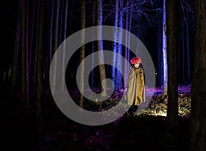 a scary evil clown wearing a dirty costume in the woods at night