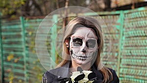 Scary girl with make-up on a halloween with a bouquet of black flowers.