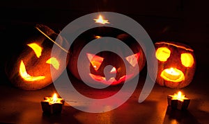 Scary halloween pumpkin and melon jack-o-lanterns on black background lit with small round and star candles