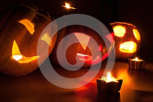 Scary halloween pumpkin and melon jack-o-lanterns on black background lit with small round and star candles