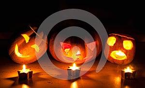 Scary halloween pumpkin and melon jack-o-lanterns on black background lit with small round and star candles