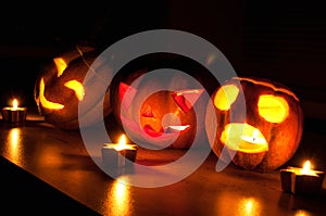 Scary halloween pumpkin and melon jack-o-lanterns on black background lit with small round and star candles