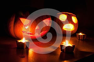 Scary halloween pumpkin and melon jack-o-lanterns on black background lit with small round and star candles