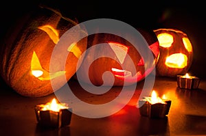 Scary halloween pumpkin and melon jack-o-lanterns on black background lit with small round and star candles