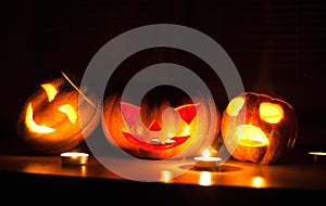 Scary halloween pumpkin and melon jack-o-lanterns on black background lit with small round and star candles