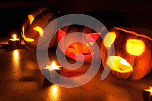 Scary halloween pumpkin and melon jack-o-lanterns on black background lit with small round and star candles