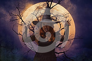 Scary halloween witch standing over dead tree, full moon and spooky cloudy sky